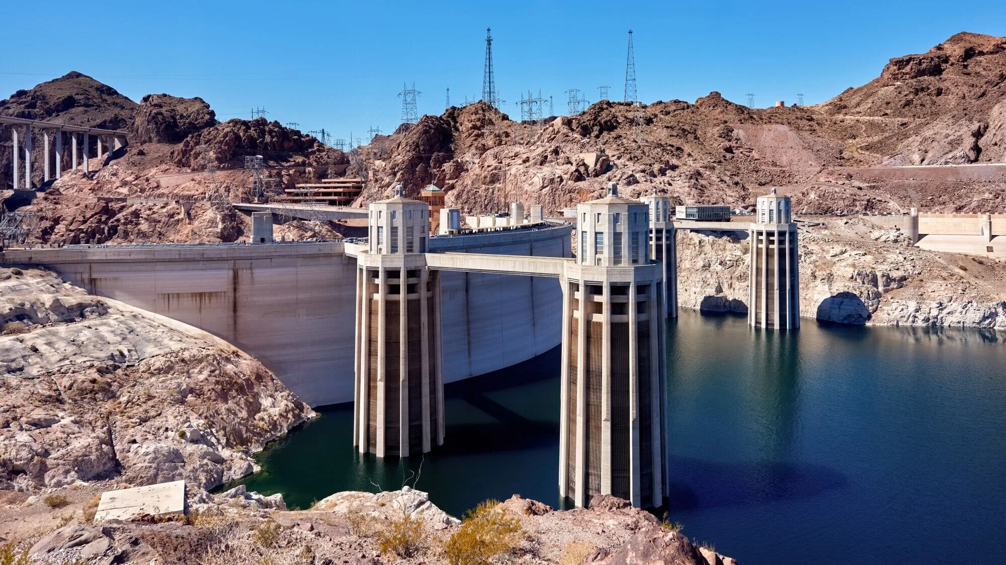 Pilhas de rejeitos na mineração. A imagem contem um céu azul e grandes pilares em meio a uma barragem de mineração. A imagem é composta por tons de azul, marrom, bege e preto.