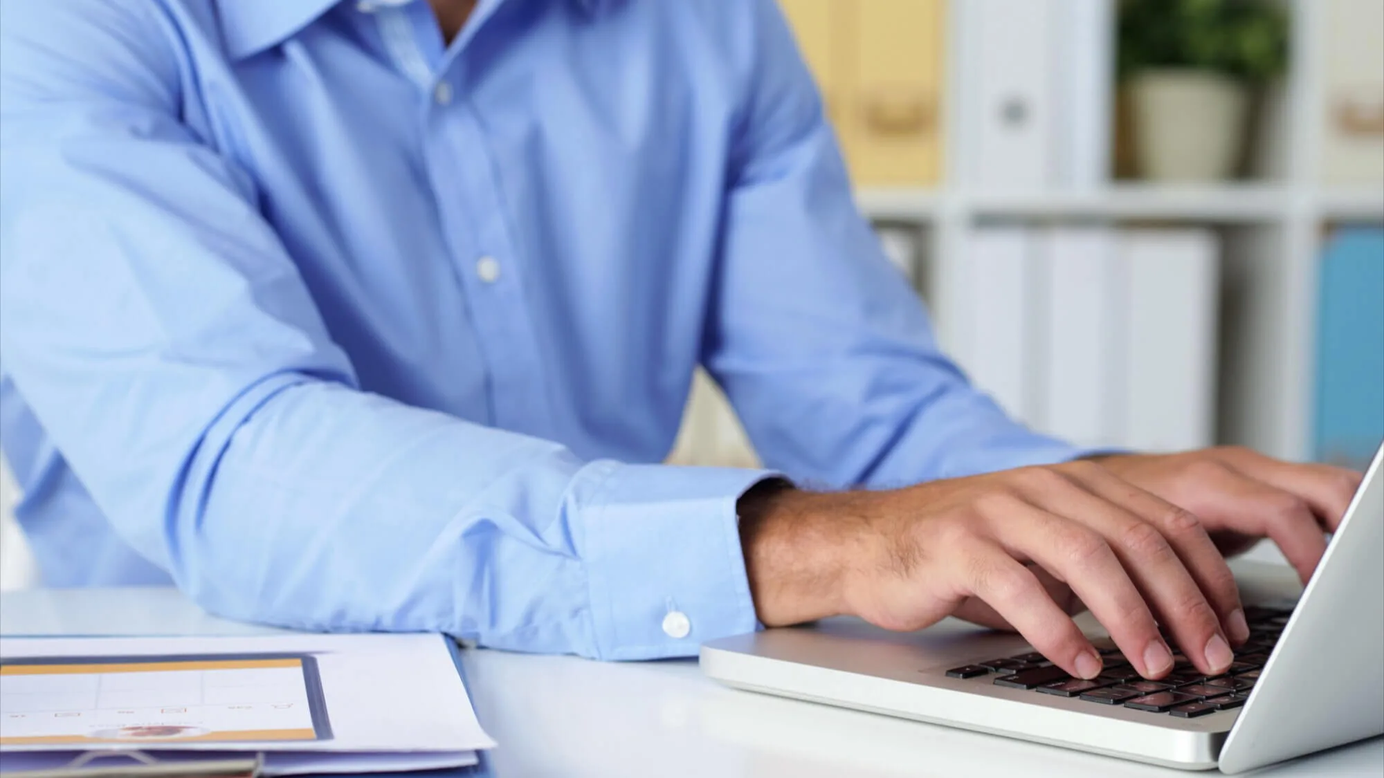 CAL, software de requisitos legais. Homem de blusa azul clara digitando no notebook em uma mesa branca.
